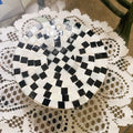 Handmade black and white checkered mosaic plant stand with three legs, designed to hold potted plants stylishly.