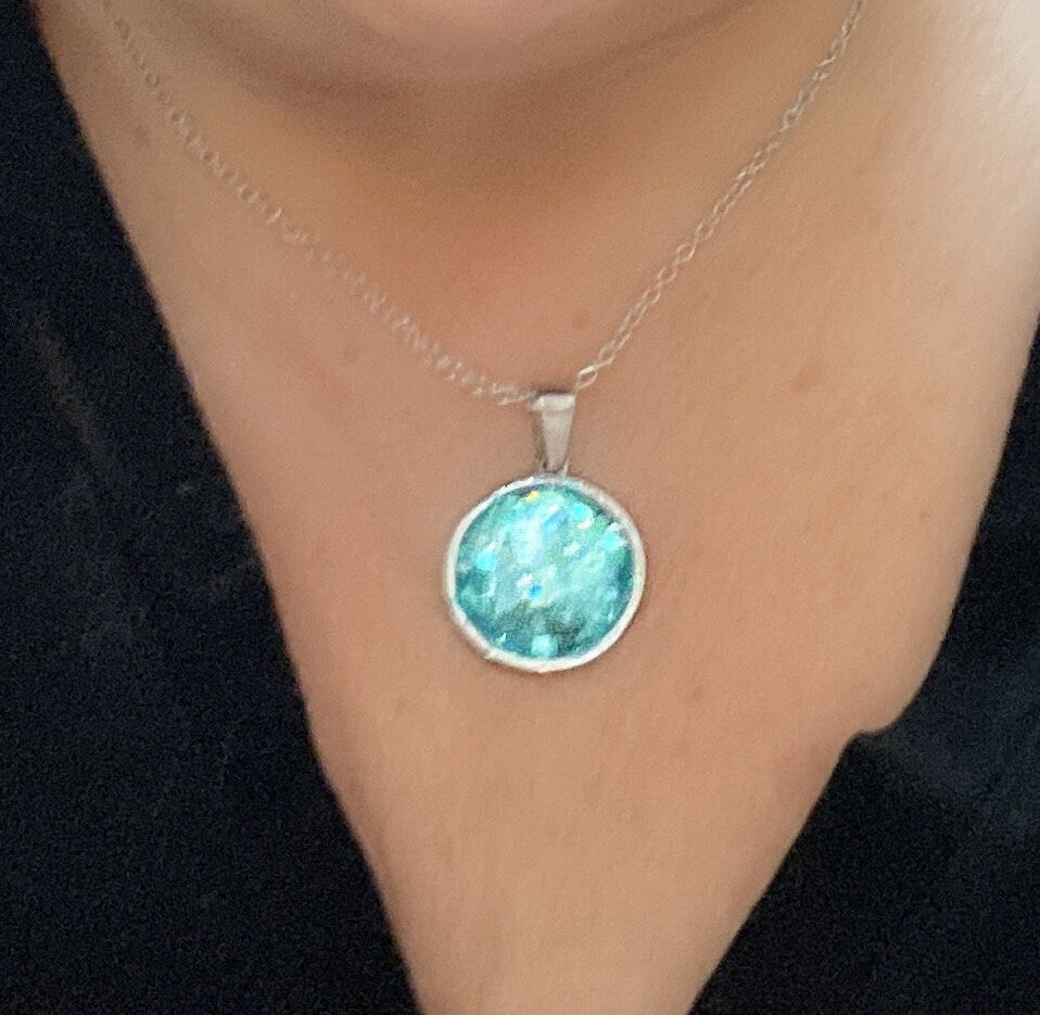 Teal blue crushed glass and silver round pendant necklace with a sleek chain, stylish jewelry piece for women.