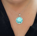 Teal blue crushed glass and silver round pendant necklace with a sleek chain, stylish jewelry piece for women.