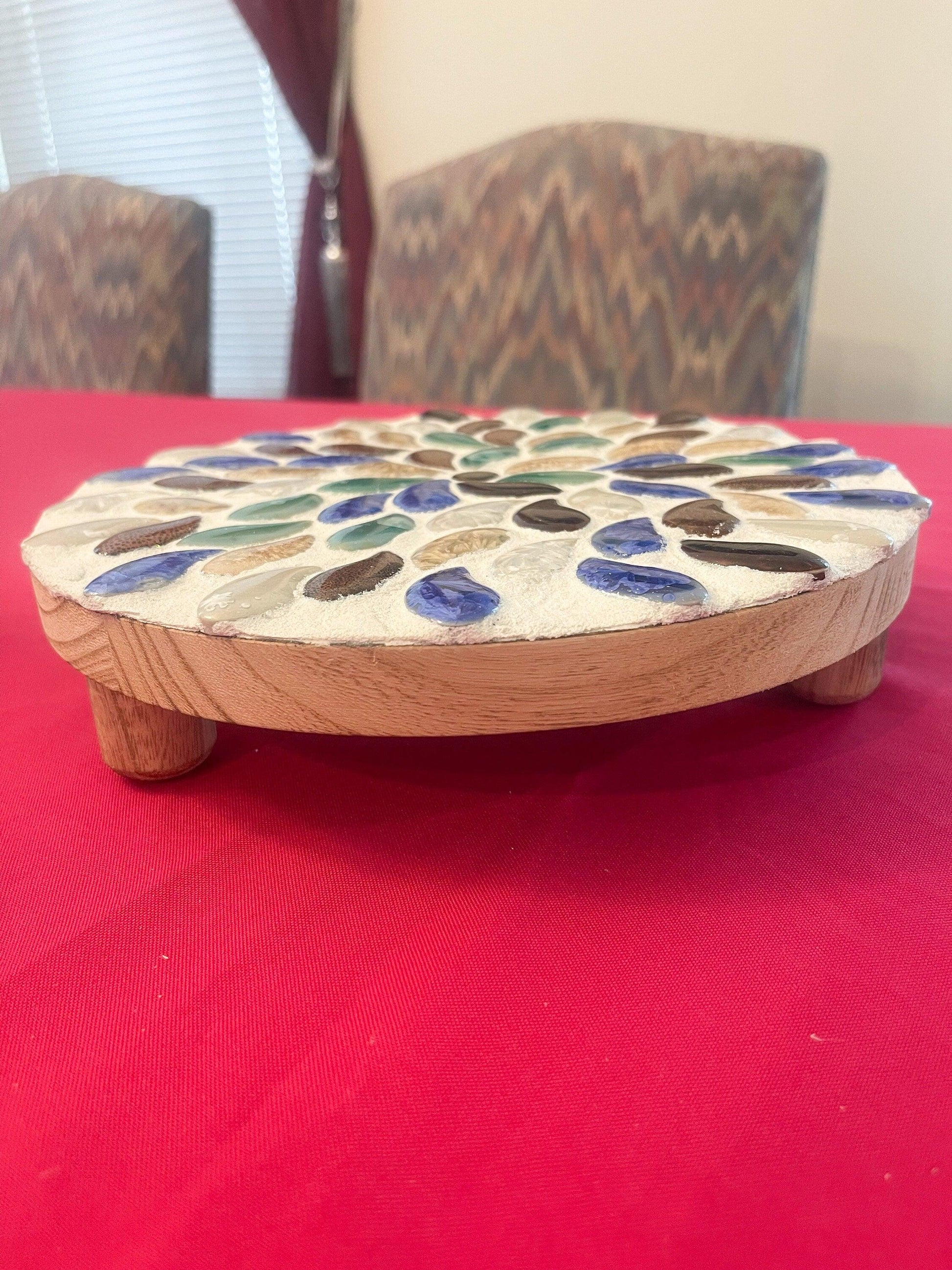 Handmade earth tone mosaic plant stand with colorful ceramic tiles, designed to hold potted plants in a stylish indoor or outdoor space.