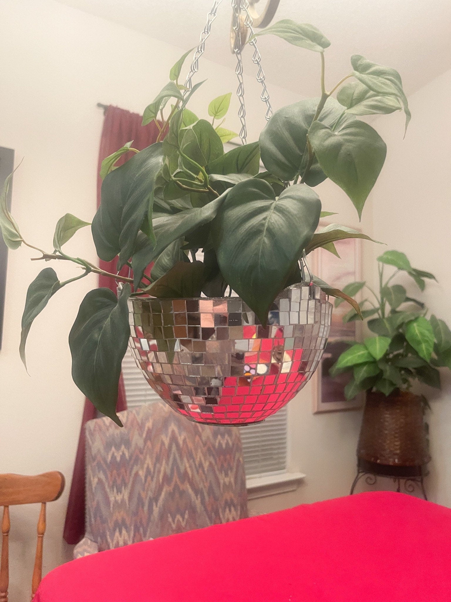 Hanging disco ball planter by Miss Bette's Creations with artificial pink carnations inside, reflecting colorful light.