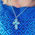 Sparkling blue crystal cross necklace with silver chain, elegant jewelry featuring a shimmering blue gemstone cross design.